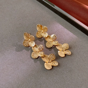 Macro detail of golden triple-layered floral drop earrings with vintage brass finish