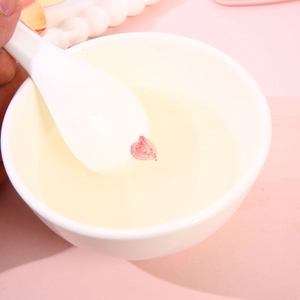 Close-up of a ceramic spoon lifting a pink heart-shaped gel floating in a white bowl