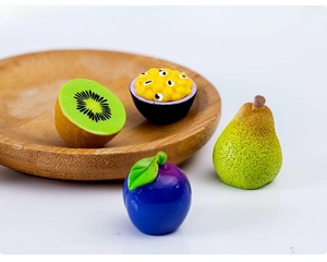 Macro detail of miniature resin fruit models including kiwi and pear on a wooden tray
