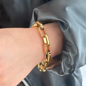 Detail shot of a minimalist gold link chain bracelet worn against a black leather sleeve