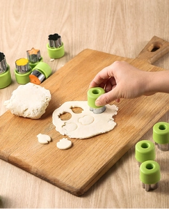 Action shot of using green handled stainless steel cookie cutter on dough in kitchen