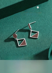 Macro detail of geometric s925 silver earrings with brown enamel on textured paper