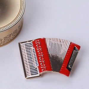 Detail of red and white enamel accordion brooch with gold metal accents on grey desk