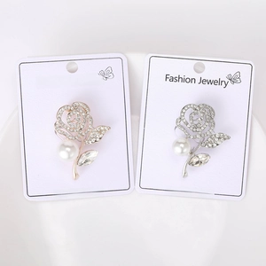 Close-up of rose gold and silver rhinestone rose brooches with pearls on a card
