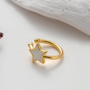 Detail of gold cartilage ear cuff with white enamel star charm on minimalist white prop