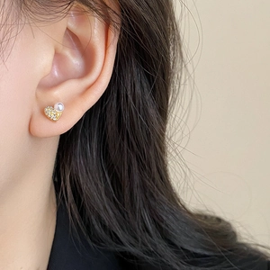 Gros plan sur boucle d'oreille cœur doré avec petits cristaux et perle portée