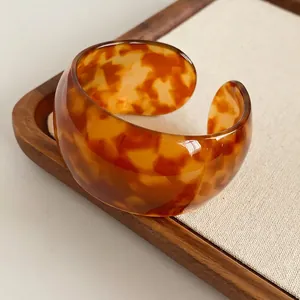 Polished tortoiseshell acetate open bangle with amber textures on linen display tray