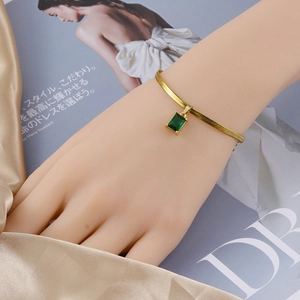 Detalle de una pulsera de cadena de serpiente dorada con un colgante de gema verde rectángular