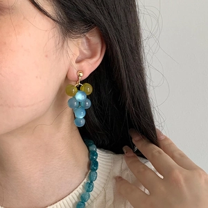 Close-up detail of a model wearing elegant resin grape tassel earrings with blue beads.