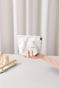 Detail of cream striped makeup bag with heart embroidery and gold flower zipper pull