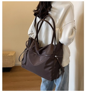 Detail of a large brown nylon tote bag with a front zipper pocket worn by a model