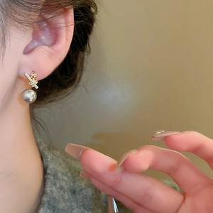 Close-up of elegant gold knot earrings with sparkling cubic zirconia and gray pearl charm