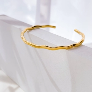 Detailed view of a gold wavy open cuff bracelet resting on a geometric white prism