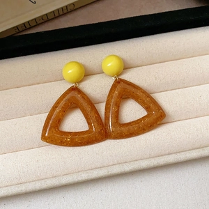 Macro shot of yellow resin stud earrings with amber triangle pendants and gold foil