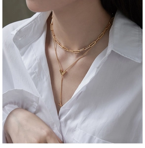 Detail of layered gold V pendant necklace with paperclip chain on a model's neck