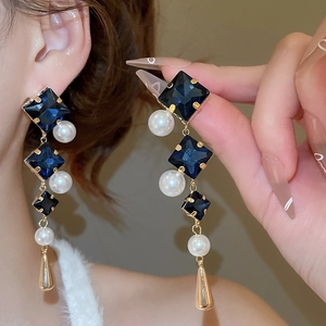Close-up of dangling earrings with navy blue crystals, white pearls and gold teardrops