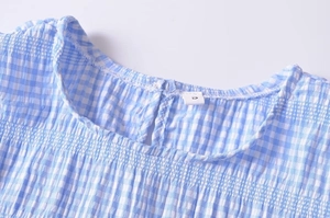 Close-up of blue plaid top featuring a pleated round neckline and back button closure