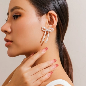 Detail of bow-shaped faux pearl earrings with elegant tassel design on a female model