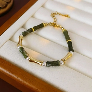 Detail of bamboo shaped green stones and white pearls on a gold link necklace chain