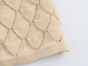 Macro view of beige knit cardigan showing hollow diamond pattern and ribbed hem detail