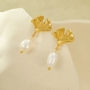 Elegant 18K gold ginkgo leaf earrings featuring white freshwater pearl drops on a beige stand