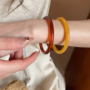 Detail view of stacked amber and yellow resin bangle bracelets worn with linen clothing
