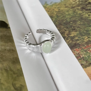 Detailed macro view of an oval green gemstone set in a ribbed silver open ring band