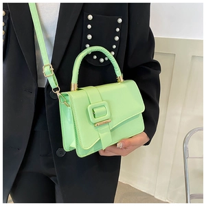 Close-up of a mint green crossbody bag with decorative square buckle on a model