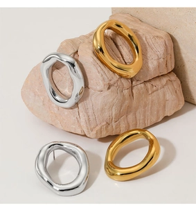 Close-up of irregular oval earrings in gold and silver finish on a textured stone