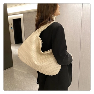 Detail view of beige woven leather shoulder bag styled with a professional black blazer