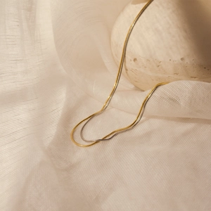 Close-up of dual-tone gold and silver snake bone chain necklaces on a textured stone