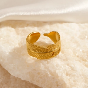 Adjustable golden stainless steel feather ring placed on white crystal with silk fabric