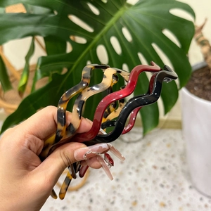 Detailed view of tortoise shell wavy hairband held by hand in a natural home setting
