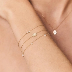 Close-up of layered gold bracelet with white pearls and star pendant on woman wrist