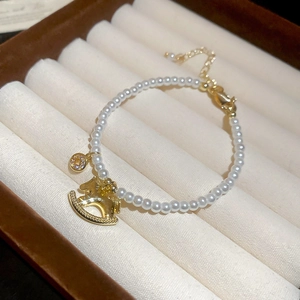 Detail of pearl bracelet with golden rocking horse charm on a jewelry display cushion