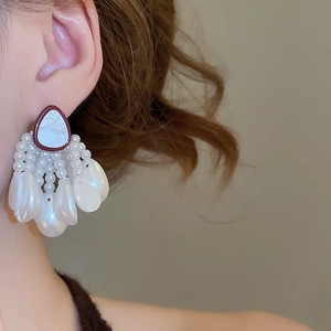 Detail of elegant shell starfish pearl tassel earrings worn by a model in warm light