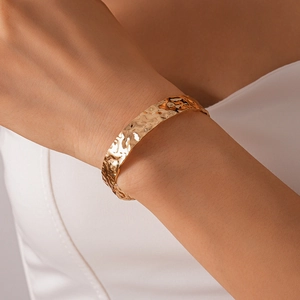 Close-up of gold open cuff bracelet with irregular hammered texture on model wrist