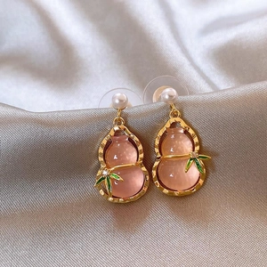 Pink gourd pearl earrings with golden bamboo leaves on luxury champagne silk background