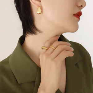 Boucles d'oreilles C dorées minimalistes et bagues texturées sur un mannequin