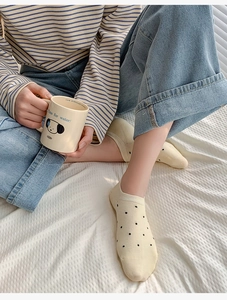 Cozy lifestyle shot of beige polka dot cotton socks with a cute cartoon mug on white linen