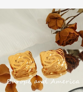 Detail of square gold earrings with spiral rose relief on a mirror with flowers