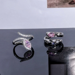 Macro shot of silver snake ring with pink marquise diamond and star pattern ring on black mirror