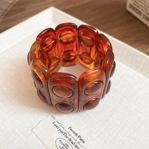 Macro detail of a wide amber resin bangle with wave pattern on a textured tray