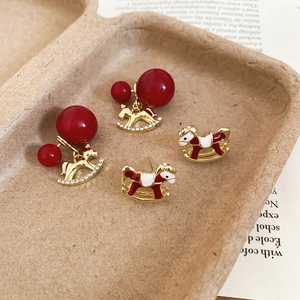 Détail de boucles d'oreilles cheval à bascule en émail rouge avec strass et accents dorés