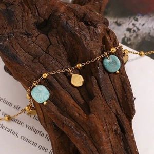 Detailed close-up of 18K gold plated anklet with shell and turquoise stone on wood