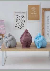 Artistic female body sculpture candles in grey, brown and blue on a wooden shelf