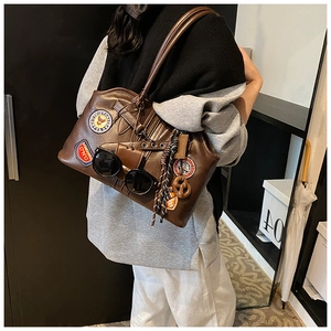 Detail der braunen Vintage-Ledertasche mit Retro-Patches und dekorativem Sonnenbrillen-Accessoire