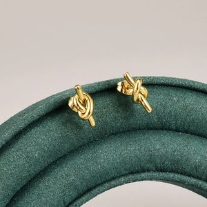 Elegant 18K gold-plated titanium knot stud earrings on a green velvet jewelry stand