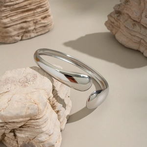 Detailed view of silver teardrop open bangle placed on natural stone for texture