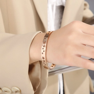 Detail view of 18K rose gold hollow star bangle on wrist with a minimalist design